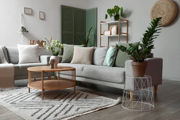 Interior of modern living room with grey sofas, flower vase on coffee table and houseplants