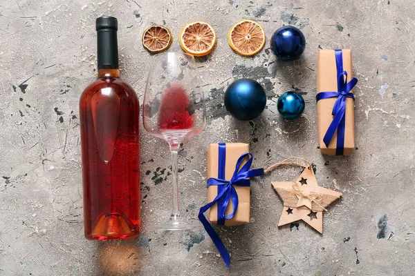 Gri arka planda Noel hediyesi kutularıyla dolu bir şişe ve bir bardak şarap.