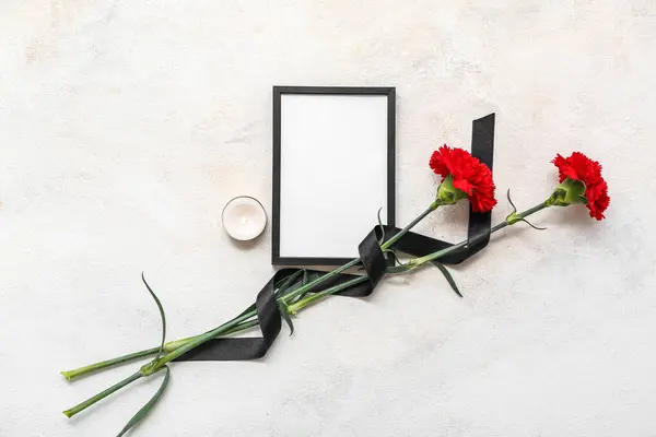Blank funeral frame, burning candle and carnation flowers on light background