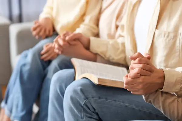 Family with Holy Bible praying on sofa at home, closeup