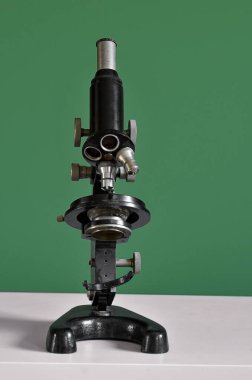 Yeşil duvarın yanındaki masada antika mikroskop var.