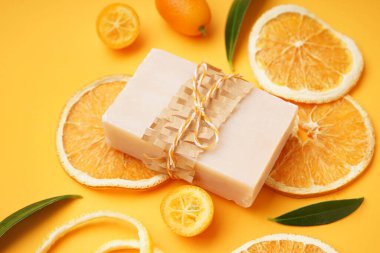 Doğal sabun kalıbı, kurutulmuş portakal dilimleri ve sarı arka planda kumkatlı kompozisyon, yakın plan.