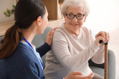 Senior woman with stick and caregiver at home clipart