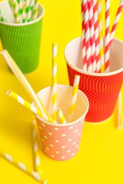 Sarı arka planda farklı pipetli kağıt bardaklar.