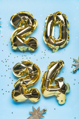 2024 numaralı altın folyo balonları ve mavi arka planda Noel yıldızları
