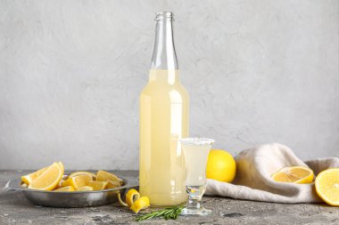 Bir şişe lezzetli limoncello ve gri masada biberiye.