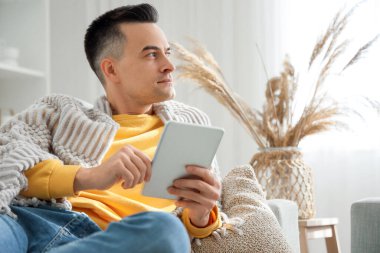 Evde tablet bilgisayar kullanan, sıcak ekoseli yakışıklı bir adam.