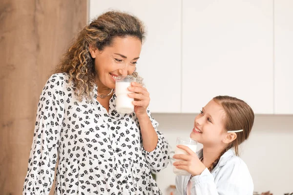 Happy mother with her little daughter drinking milk in kitchen