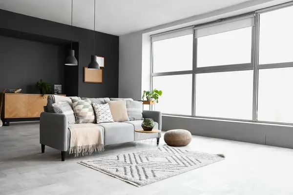 Interior of modern living room with cozy grey sofa, pouf and coffee table