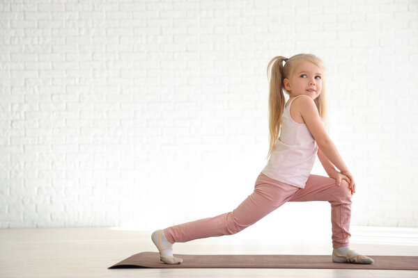 Маленькая девочка занимается гимнастикой на коврике в спортзале