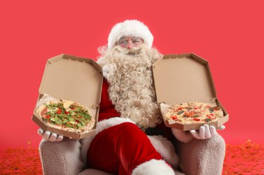 Noel Baba kırmızı arka planda koltukta lezzetli pizza kutularıyla