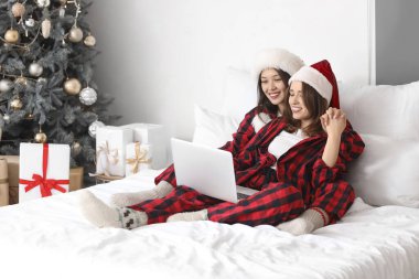 Noel arifesinde yatak odasında dizüstü bilgisayarı olan genç lezbiyen çift
