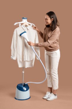 Güzel, genç bir kadın. Kahverengi arka planda modern buharlı giysiler.