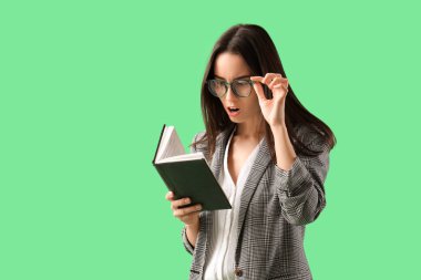 Gözlüklü genç iş kadını, yeşil arka plan üzerine kitap okuyor.