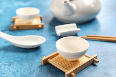 Mavi grunge arka planda fincanlı çaydanlık, kase ve çubuklar, yakın plan. Çin masa ayarları