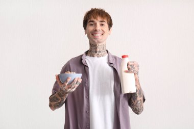 Mısır gevreği halkaları ve beyaz desenli arka planda bir şişe süt taşıyan bir adam.