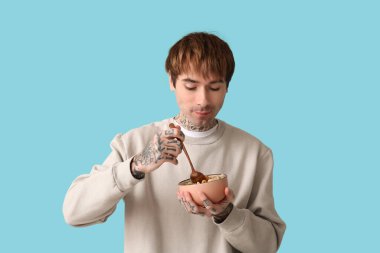 Elinde mısır gevreği halkaları ve mavi arka planda kaşık tutan adam.