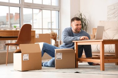 Evde dizüstü bilgisayar kullanan paketli genç bir adam.