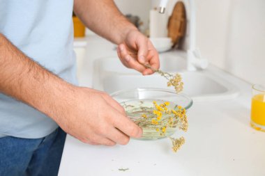 Genç adam mutfaktaki masada otlarla buhar solunumu hazırlıyor.