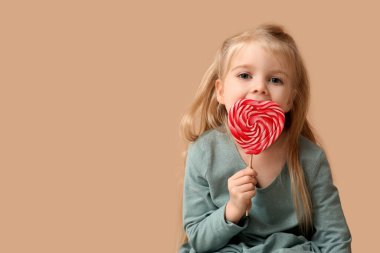 Bej arka planda kalp şeklinde lolipopu olan tatlı küçük bir kız. Sevgililer Günü kutlaması