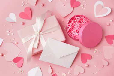 İçinde hediye kutuları, kağıt kalpler ve pembe arka planda dekorasyon olan bir zarf. Sevgililer Günü kutlaması