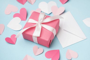 Zarfın içinde hediye kutusu ve mavi arka planda kağıt kalpler var. Sevgililer Günü kutlaması