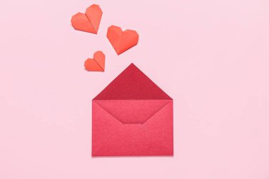 Zarflı kompozisyon ve pembe arka planda kırmızı kağıt kalpler. Sevgililer Günü kutlaması