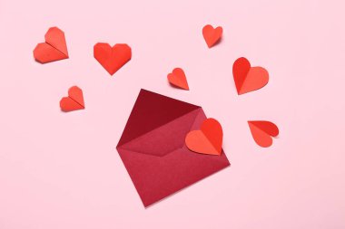 Zarflı kompozisyon ve pembe arka planda kırmızı kağıt kalpler. Sevgililer Günü kutlaması