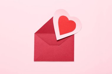 Zarflı kompozisyon ve pembe arka planda kırmızı kağıt kalp. Sevgililer Günü kutlaması