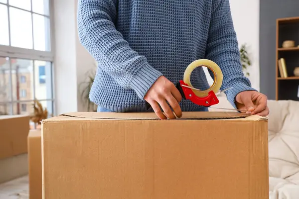 Young man packing parcel box with tape at home, closeup