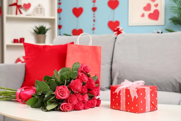 Bouquet of beautiful roses and gift box on coffee table in living room, closeup. Valentine\'s Day celebration