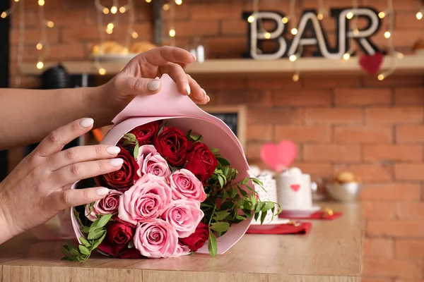 Woman with bouquet of beautiful roses on wooden table, closeup. Valentine\'s Day celebration
