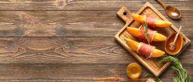 Cutting board with tasty melon, prosciutto, rosemary and honey on wooden background with space for text