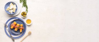 Tasty melon with prosciutto, cheese, olives and honey on light grunge background with space for text