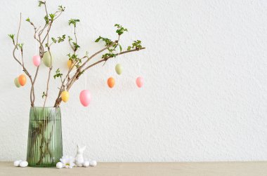 Ağaç dalları ve Paskalya yumurtaları olan vazo ışık duvarının yanında.