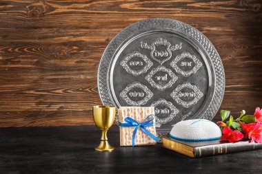 Passover Seder plate, flatbread matza, cup, Torah and kippah on dark table