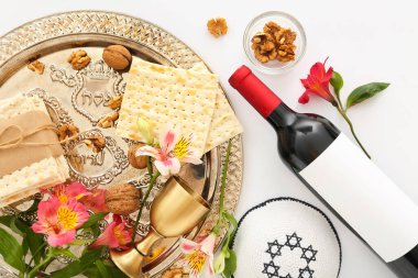 Passover Seder plate with flatbread matza, walnuts, bottle of wine, kippah and flowers on white background, closeup