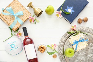 Frame made of Passover Seder plate, flatbread matza, wine, Torah and flowers on white wooden background