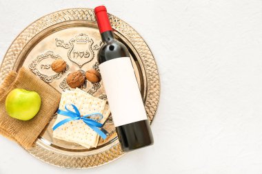 Passover Seder plate with flatbread matza, bottle of wine, apple and walnuts on light background
