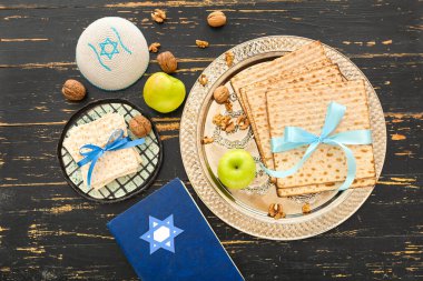 Passover Seder plate with flatbread matza, Torah, kippah, apples and walnuts on dark wooden background