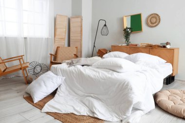 Yatak, koltuk ve yastıklı dağınık bir yatak odası.