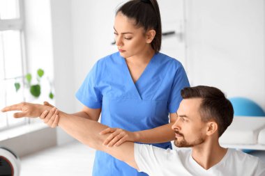 Rehabilitasyon merkezinde tekerlekli sandalyedeki genç adamla çalışan kadın fizyoterapist.