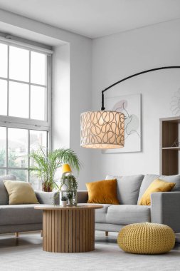 Işıl ışıl oturma odasının içinde rahat gri koltuklar, sehpa ve büyük pencerenin yanında parlayan lambalar.