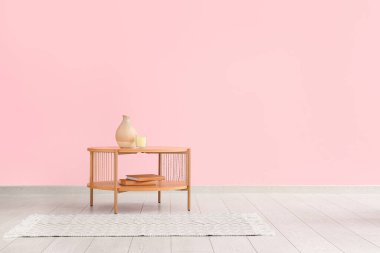 Vazo, mum ve pembe duvarın yanında kitaplar olan ahşap sehpa.