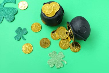 Pots with coins and paper clovers on green background. St. Patrick's Day celebration