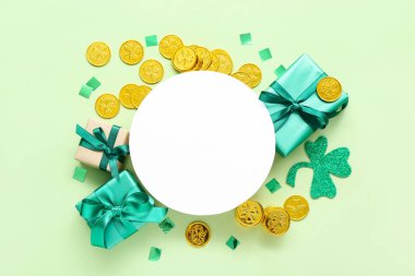 Blank round card with gifts, golden coins and paper decor on light green background. St. Patrick's Day celebration