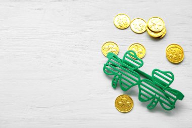 Eyeglasses and golden coins on white wooden background. St. Patrick's Day celebration