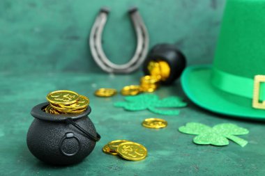 Pots of golden coins and paper clovers with leprechaun hat and horseshoe on green grunge background. St. Patrick's Day celebration