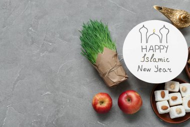 Card with text HAPPY ISLAMIC NEW YEAR, sweets, grass and apples on grunge background