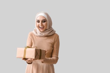 Young Muslim woman with gift on light background. Islamic New Year celebration